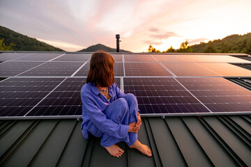 Rooftop with solar panels on house in mountains, woman sitting alone raising hands and enjoying...
