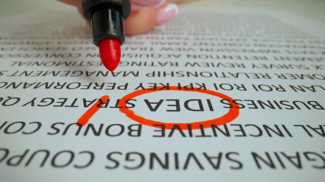 Close up shot of woman hand working with document, red marker in female hand marked circled a word idea with exclamation mark in text.