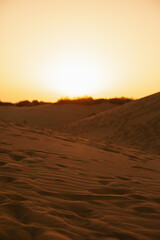 sunset in the desert, sandy dunes closeup, orange sky, backlit vertical landscape, traces on sand. Gran Canaria, Canary Islands, Spain.