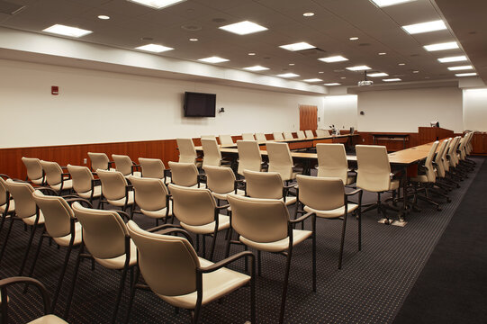 Interior view of a lecture hall or meeting room, a large conference table with a monitor screen on the wall.