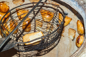 The process of removing freshly baked delicious beautiful pies called somsa and samsa from the walls of a large stone oven - tandoor. Asian cuisine and cooking equipment.