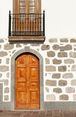 old wooden door in white building decorated with volcanic stones with traditional wooden balconies in Tejeda village, Gran Canaria island, Canary Islands, Spain. Traditional architecture. 