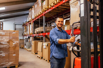 A young smiling man in a warehouse with a forklift truck. An attractive worker in casual clothes...