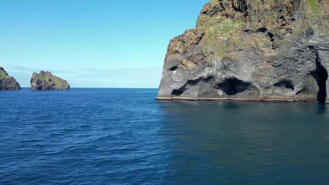 A drone image of Elephant Rock in Iceland. The striking basalt formation resembles an elephant's head dipping into the deep blue ocean, with clear skies adding to the stunning natural beauty. 4K