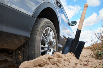 A car stuck in the sand with a shovel placed nearby, ready for use. The image captures a close-up...