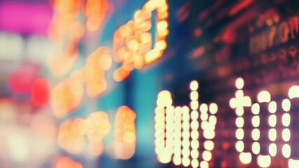A blurred close-up of a neon stock market ticker display illuminates a busy urban setting. The glowing orange and red lights stand out in the evening, representing financial data trends. - Powered by Adobe