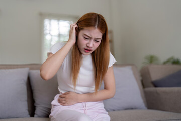 Young Woman Experiencing Stomachache While Sitting on Couch at Home, Expressing Pain and Discomfort