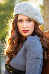 Portrait of a smiling beautiful young woman wearing a grey beret, with her long brown hair back lit by the late afternoon sunlight. 