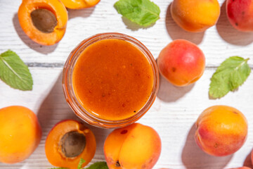 Homemade sweet sour apricot chutney jam preserves with spices and raisins, in small jar, with fresh ripe apricots on white wooden table