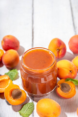 Homemade sweet sour apricot chutney jam preserves with spices and raisins, in small jar, with fresh ripe apricots on white wooden table