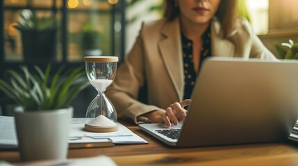 Unknown businesswoman sit at desk working on laptop, focus on hourglass showing passage of workday time. Deadline, time is money, billable hours, productive and effective work day
