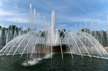 City fountain on one of the sites in St. Petersburg among greenery against the blue sky.