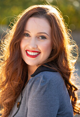 Portrait of a beautiful smiling young woman, with her long golden hair back lit by the late afternoon sunlight. 