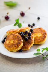 Fried curd cheese pancakes with black currants, on a wooden table