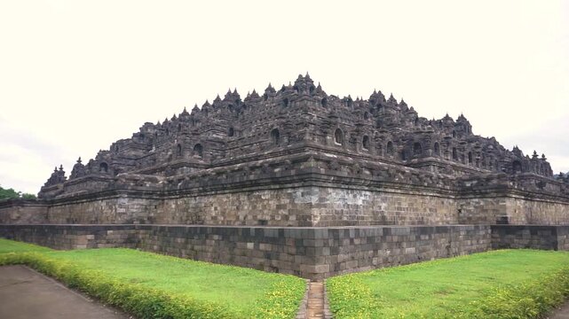 Indonesia 17 &lrm;August &lrm;2024 : wide shot of the Borobudur Temple, a massive stone structure with intricate carvings and stupas, set against a cloudy sky