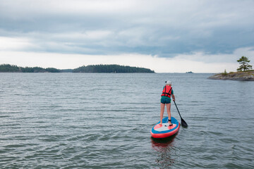 Little boy paddling on a paddle surfboard sup board in Baltic sea, Gulf of Finland, kids vacation, summer holidays in Finland