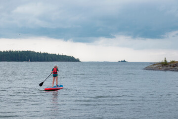 Naklejka premium Little boy paddling on a paddle surfboard sup board in Baltic sea, Gulf of Finland, kids vacation, summer holidays in Finland