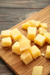 Cheese cubes on cutting board on brown background. Parmesan