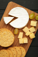 Different types of cheese with crackers on wood serving cheese board. Vertical photo