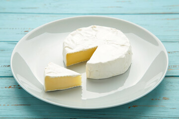 Slice camembert cheese on plate on blue wooden background.