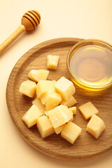 A piece of Parmesan cheese with honey on wooden plate on beige background. Vertical photo