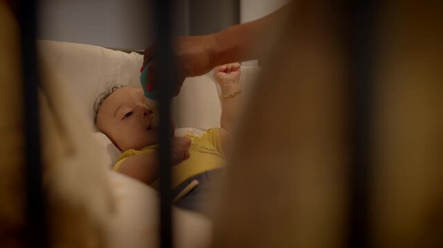 A cute baby resting peacefully in a crib, being nourished with a bottle by a caring hand