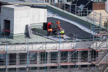 Birdseye view of roofer waterproofing the flat roof of a commercial building.