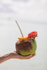 tropical refreshing coconut cocktail in female hands, ocean in the background, paradise
