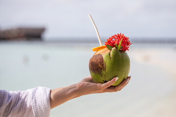 tropical refreshing coconut cocktail in female hands, ocean in the background, paradise