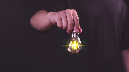 Glowing light bulb held by a male hand represents the business concepts of overcoming challenges,...