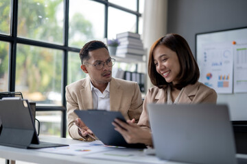 Two people are sitting at a desk with a laptop and a tablet