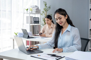 A woman is sitting at a desk with a laptop and a cell phone
