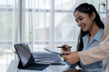 A woman is sitting at a desk with a laptop and a stack of papers