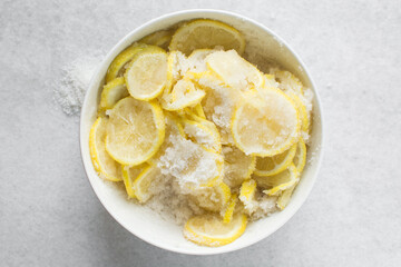 Overhead view of lemon slices and sugar being mixed together in a white bowl, process of making lemon cheong or lemon syrup