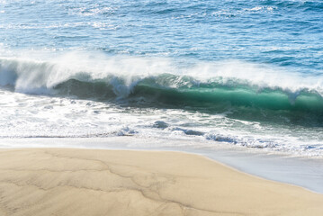 View from above of a huge wave breaking on a sandy beach in California on a sunny day