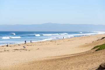 People fishing and strolling along a sandy beach in California on a misty autumn day. Huge waves are breaking on the shore.