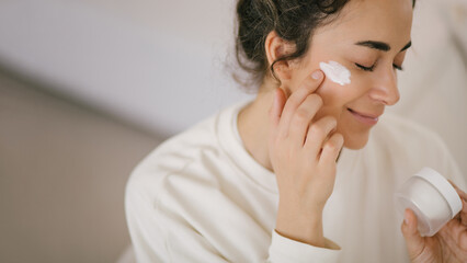 Fototapeta premium Young woman 30 years old applying face cream on her skin.
