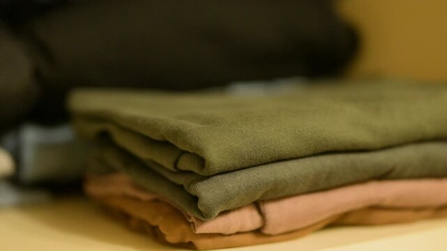 Taking t shirts from the wardrobe one by one. Stack of fresh washed clothes on the shelf