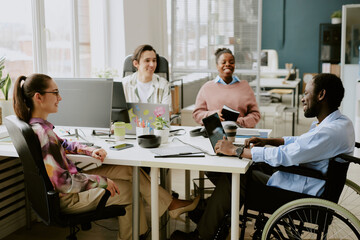 African American boss with disability looking at laptop screen while holding meeting with his biracial subordinates