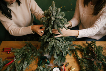 Two women making Christmas tree using natural pine branches on a workshop.