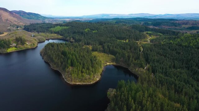 Green pine tree forest in the Trossachs National Park. Clear day on Loch Ard with rolling wooded hills. Beautiful wild landscape. Scottish Highlands, Scotland, United Kingdom.