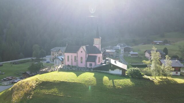 Aerial footage of Trient village in Switzerland, capturing the charming historic pink church and surrounding countryside bathed in sunlight. Trient, Switzerland, Schweiz.