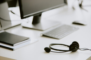 Black wired headphones on white table desk with computer and notebooks on top