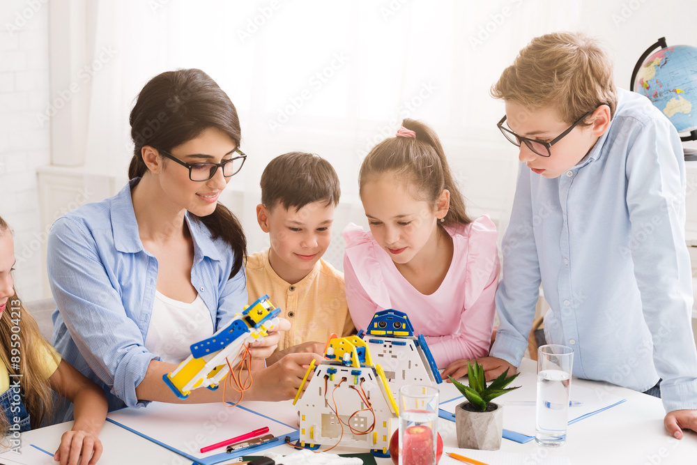 Aufkleber A teacher and four students are working together to build a robot in a classroom setting. All focused on the task at hand, with the teacher guiding the students and helping them with the assembly