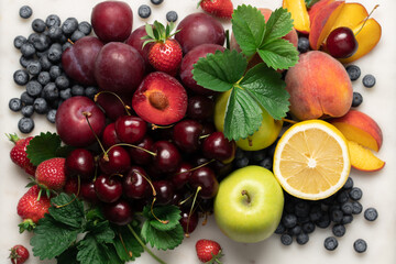 Set of summer ripe berries and fruits on a marble board, top view with copy space. Cherry, strawberry, blueberry, apples, lemon, plum, peach on a light background