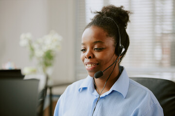 Smiling African American call center operator dressed in pastel cotton blouse speaking with client