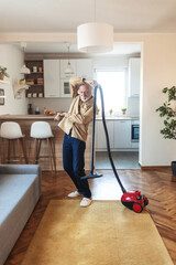 Fototapeta premium Shot of a mature man wearing headphones while vacuuming at home.