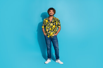Fototapeta premium Full size photo of handsome cool latin man dressed print shirt jeans standing holding arms in pockets isolated on blue color background
