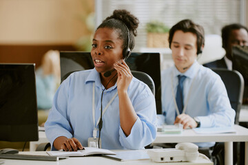African American female call center operator communication with client via headphones while coworkers working in blurred background