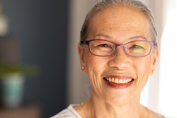 Smiling elderly asian woman wearing glasses, looking at camera indoors